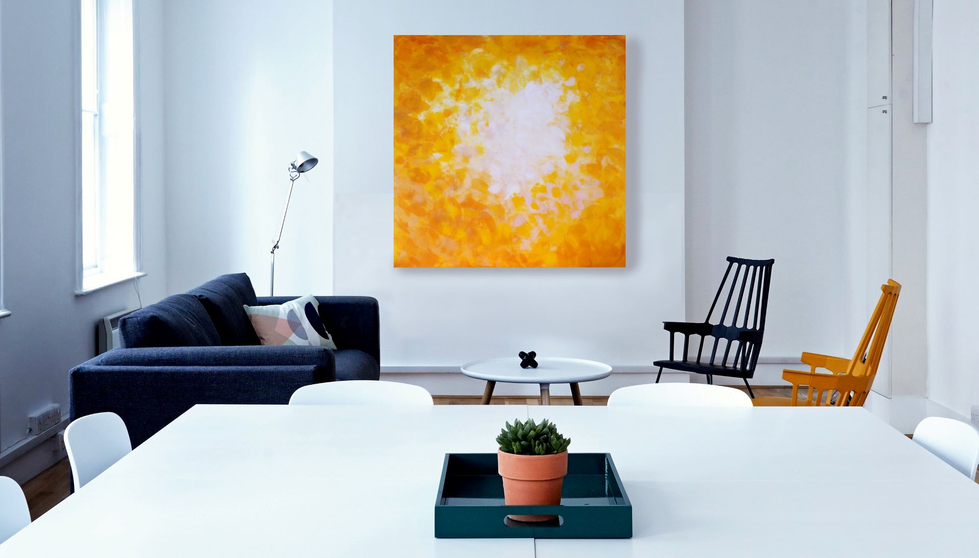 Gemälde in verschiedenen Gelb- und Weißtönen auf einer weißen Wand hinter zwei Sesseln und einem Tisch.